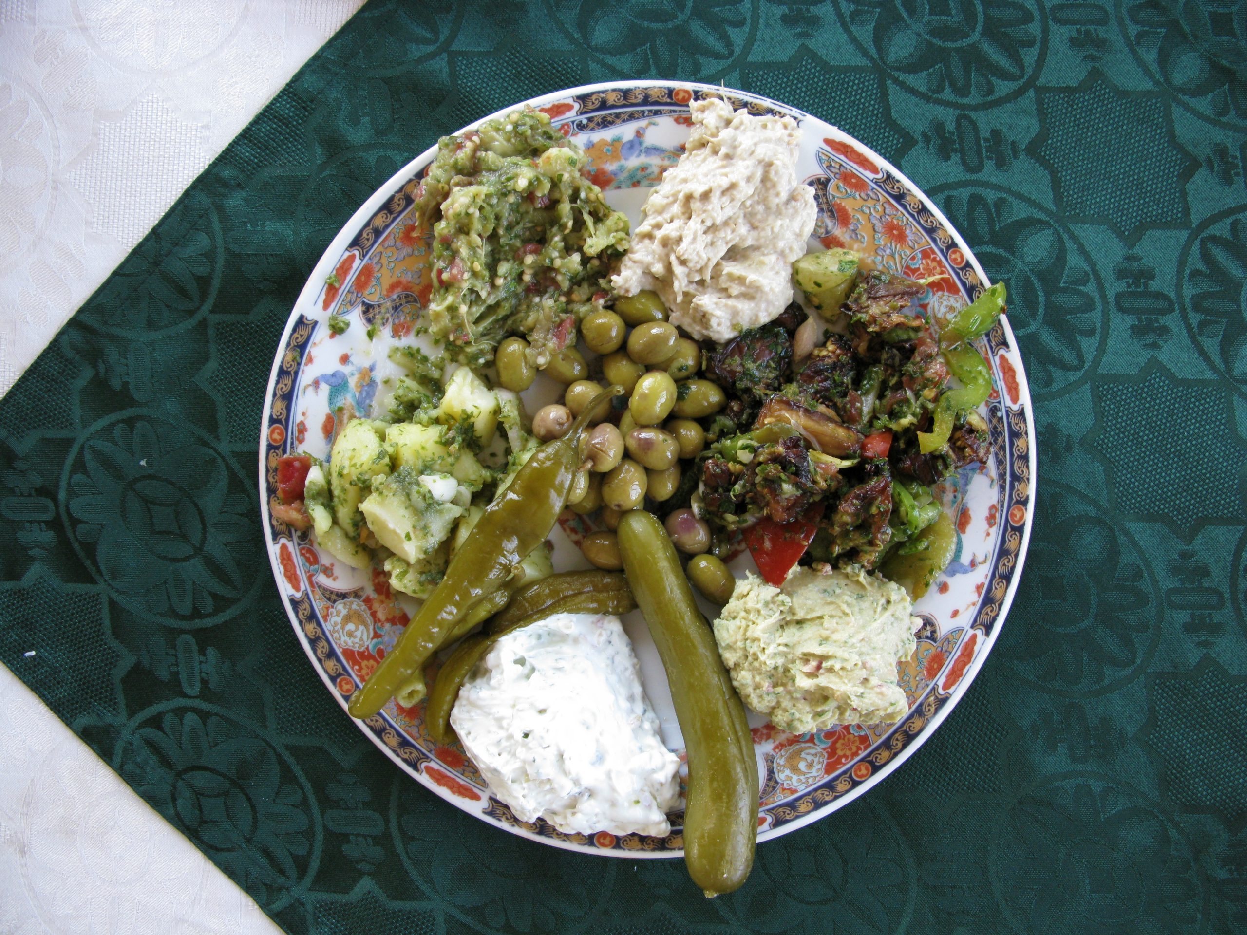 A plate of mezze with hummus, olives, pickles, salads and a yoghurt dip on a green tablecloth