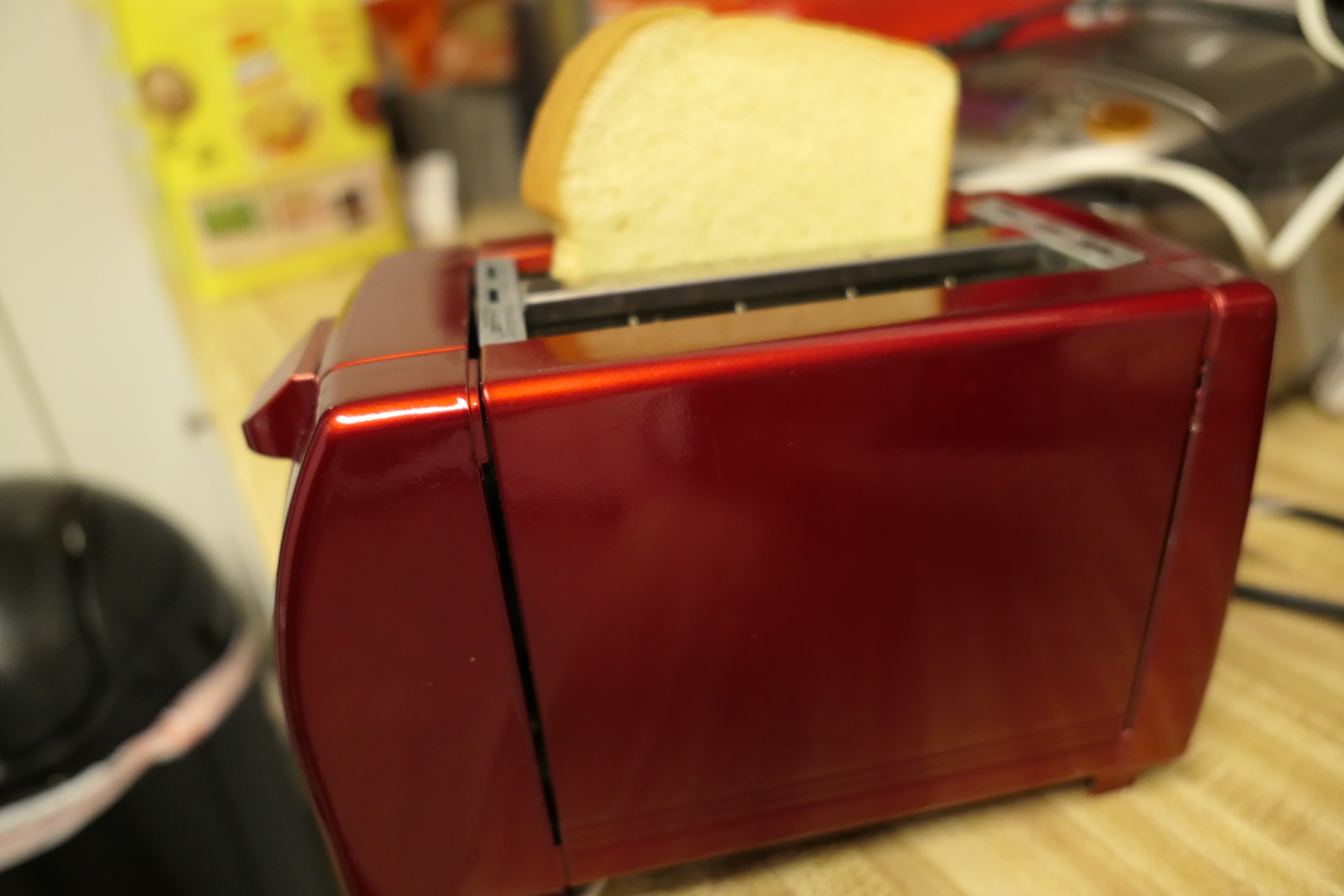 A slice of white bread sticking out of a red toaster on a kitchen worktop