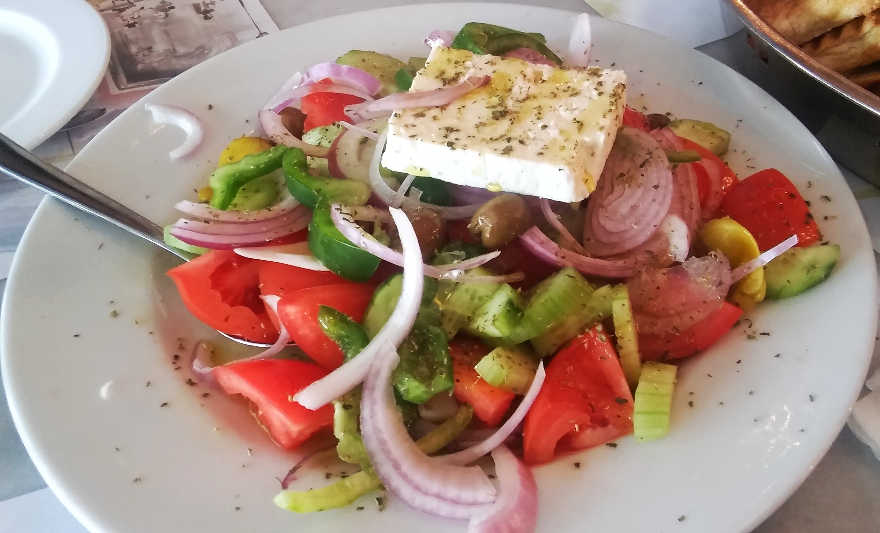 Greek salad of tomato, cucumber, peppers, red onion and olives topped with a slab of feta