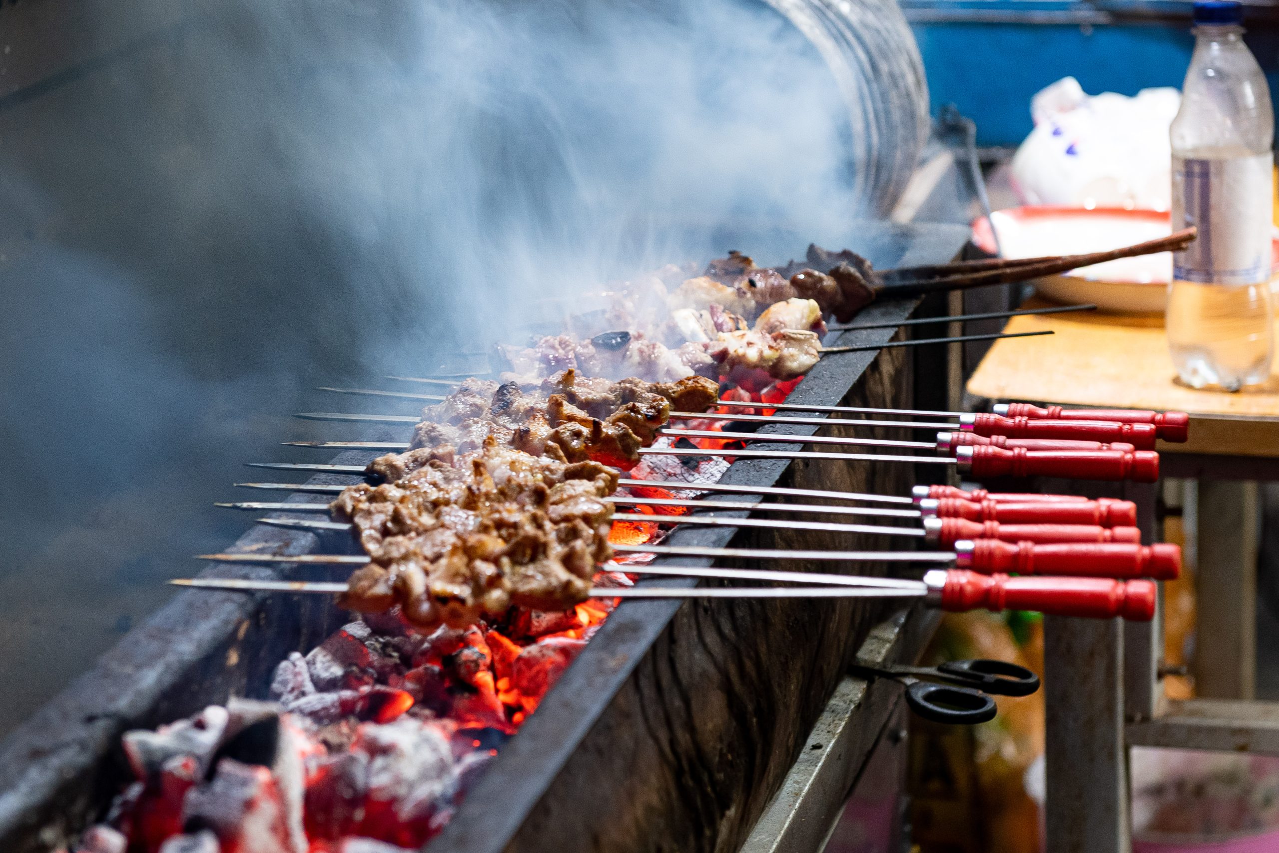 Lamb kebabs on metal skewers cooking over glowing charcoal with smoke rising