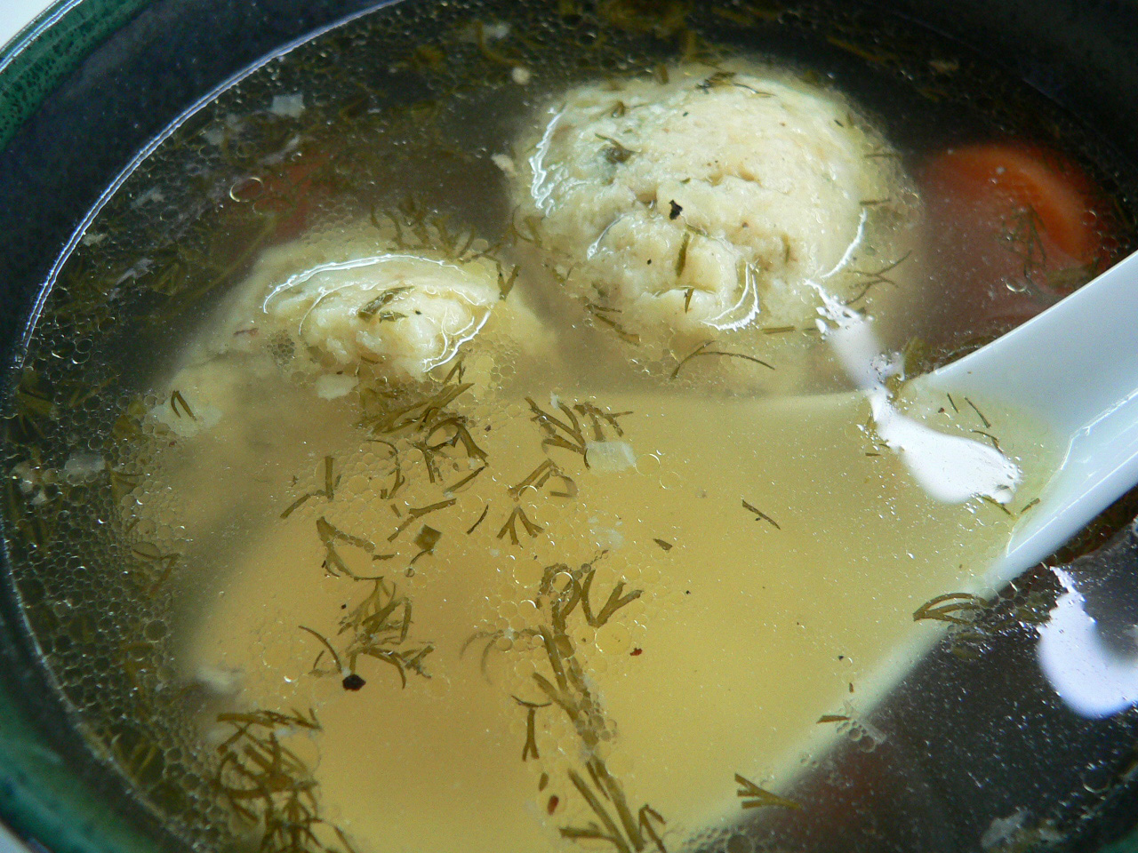 Matzo ball soup with dill and carrot in a clear broth with a white spoon