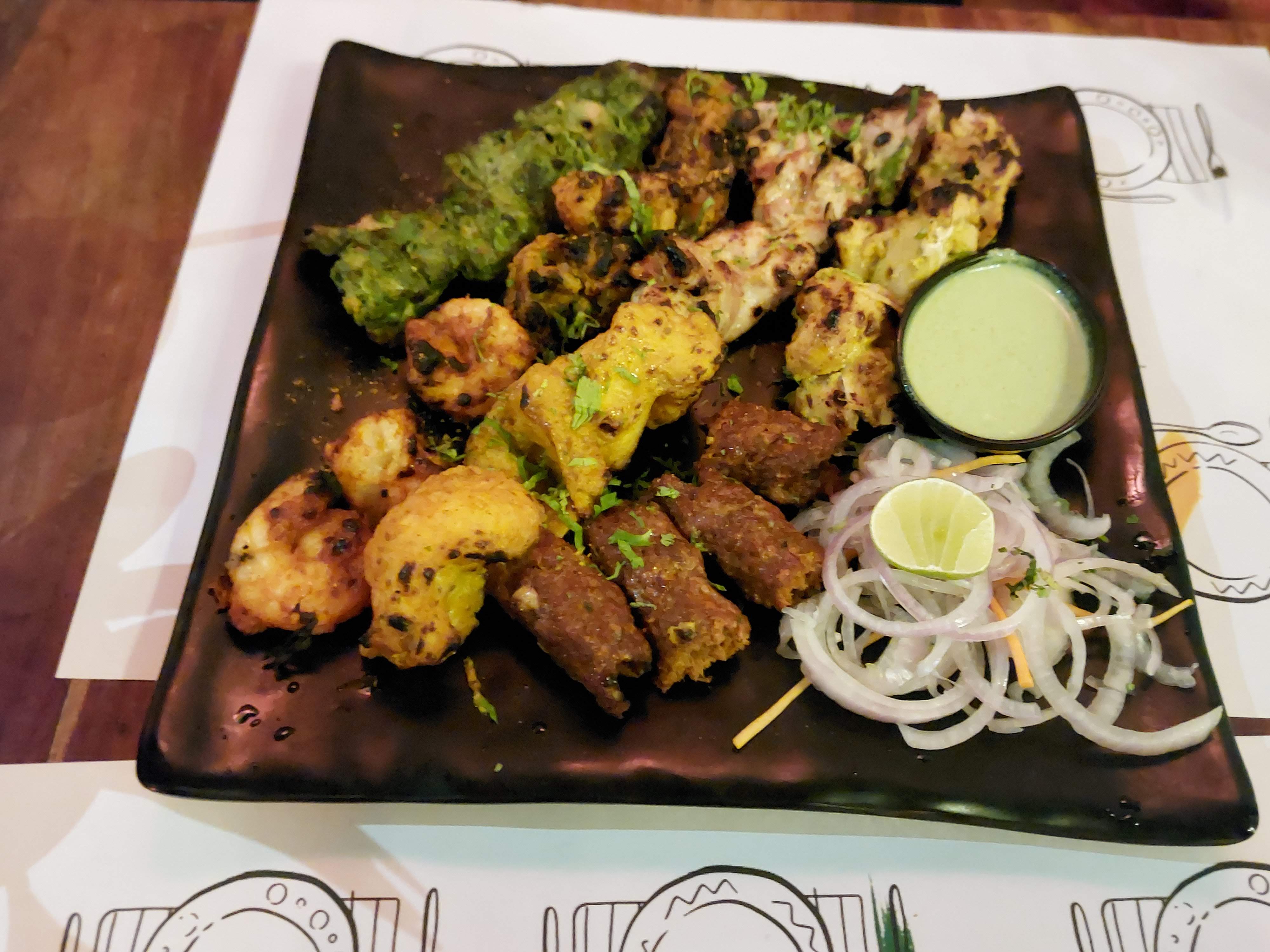 Mixed grill platter of kebabs and tikka pieces with green chutney, lime and sliced onion