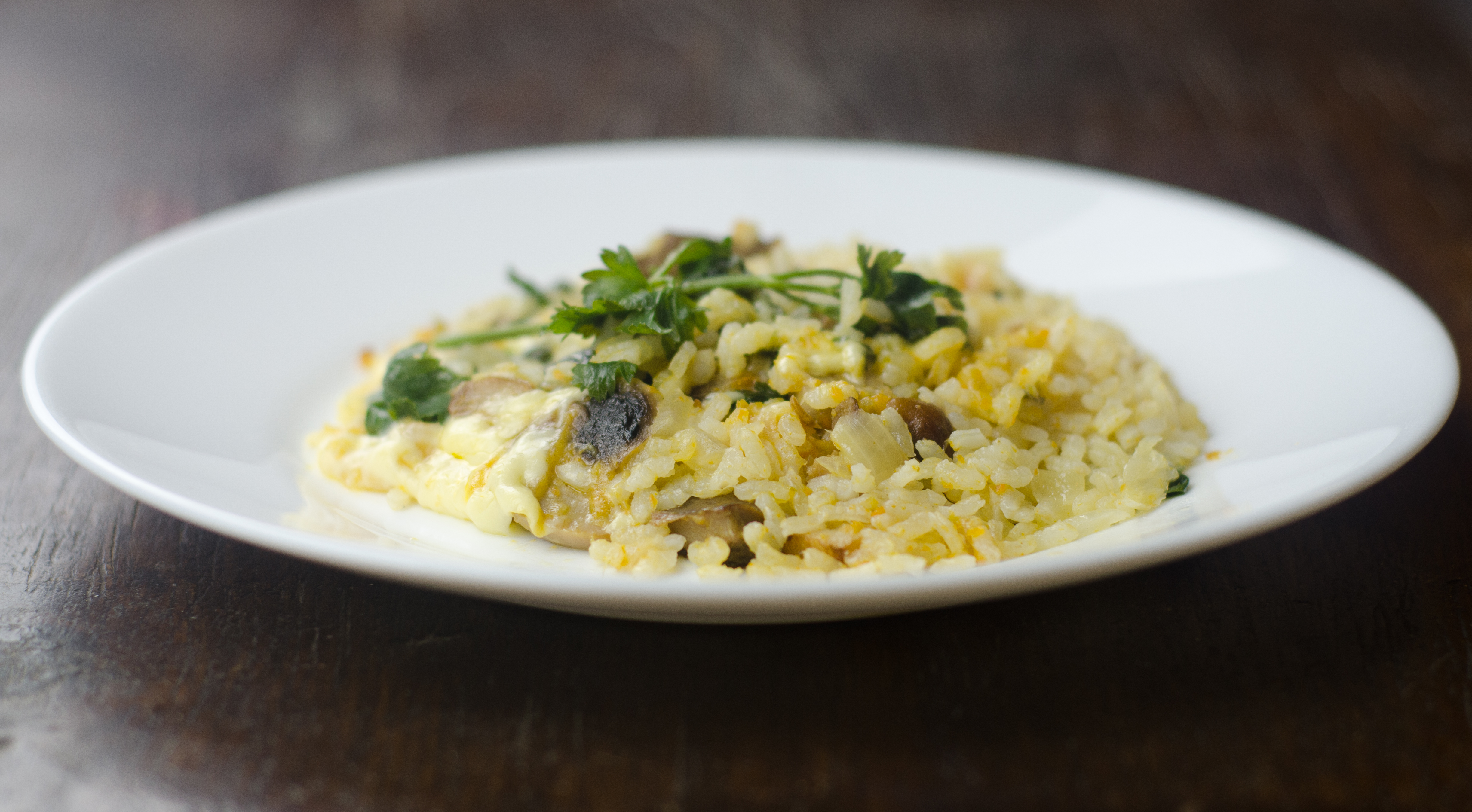 A plate of mushroom risotto topped with fresh parsley on a wooden table
