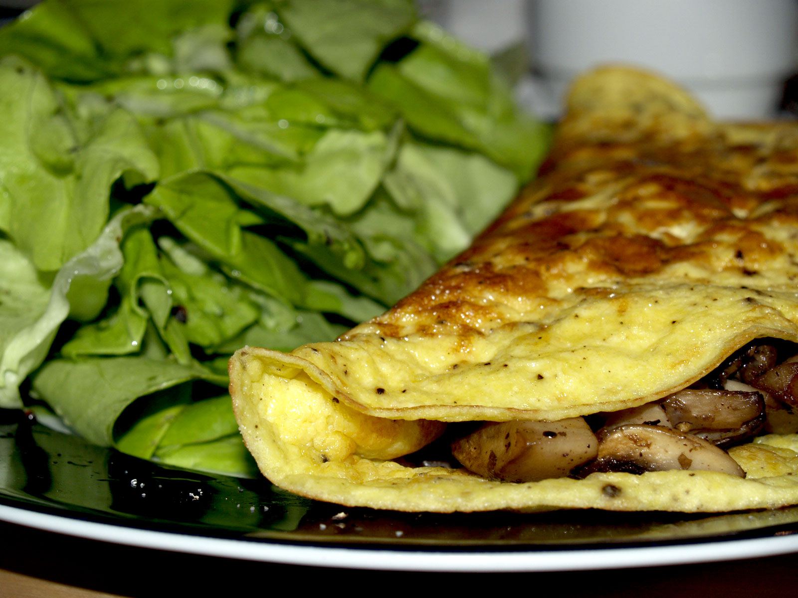 A folded mushroom omelette beside a pile of green salad leaves