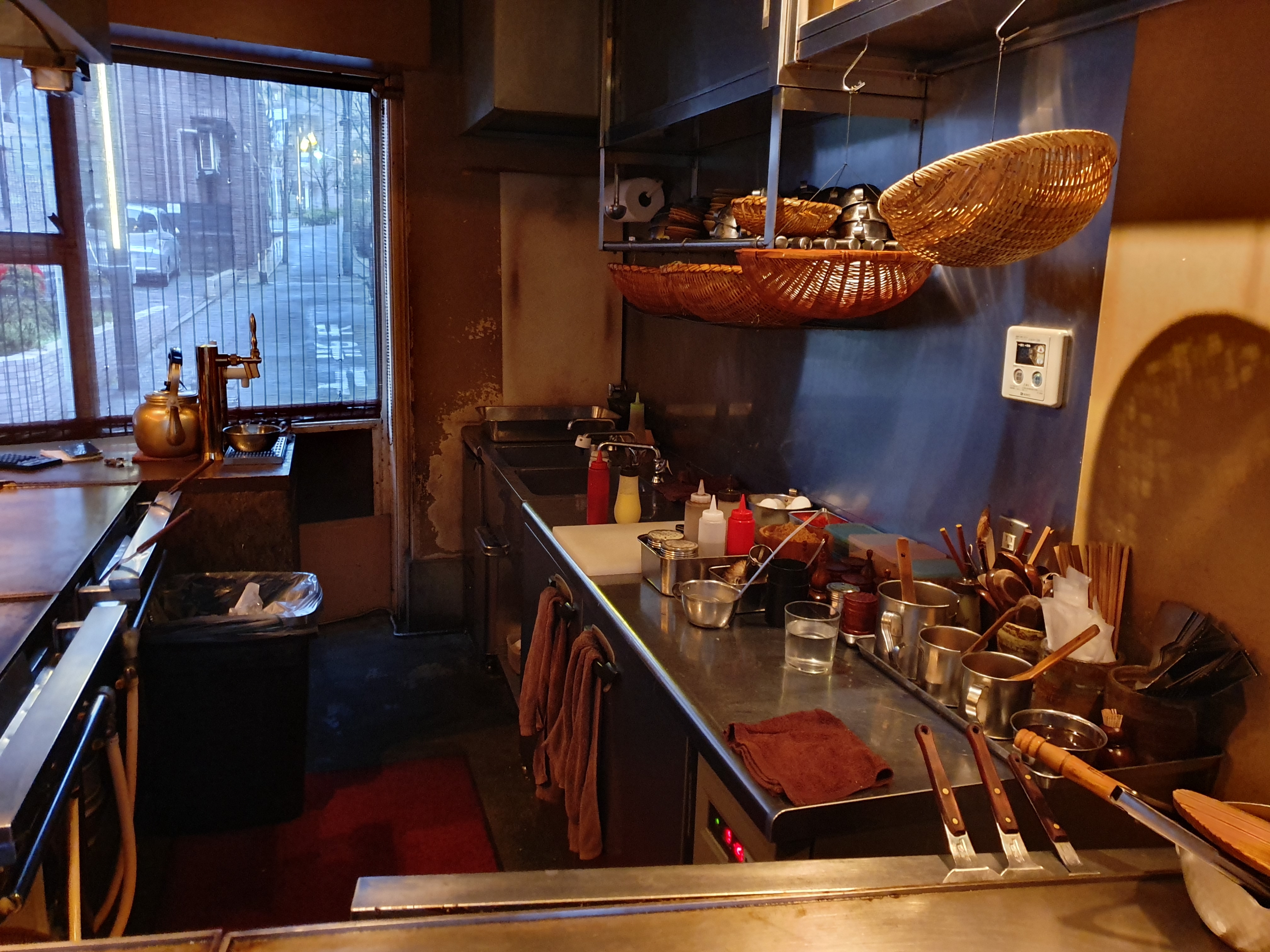 A small restaurant kitchen with a steel worktop, utensils in pots and baskets hanging above
