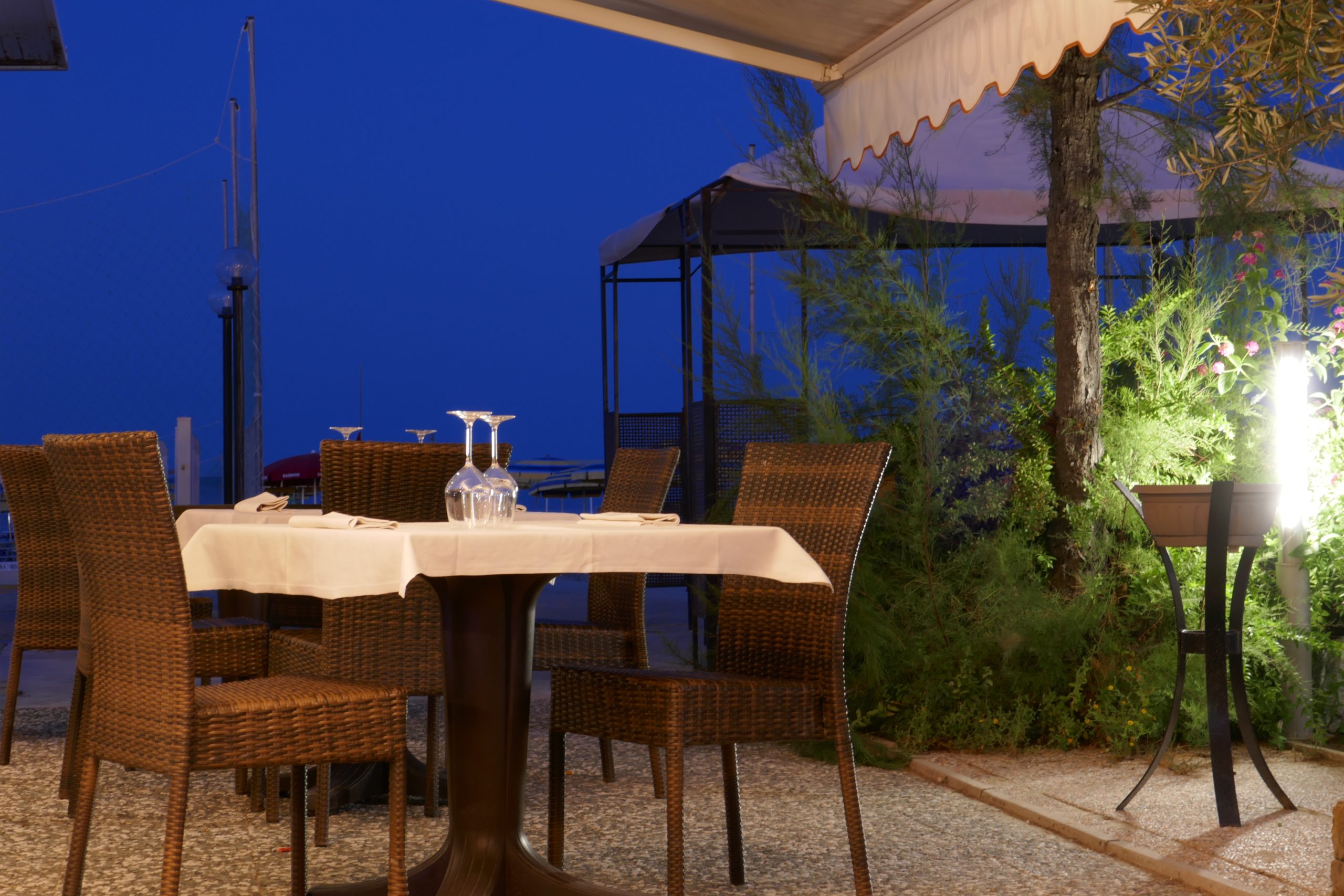 An outdoor restaurant table laid with a white cloth and wine glasses at dusk
