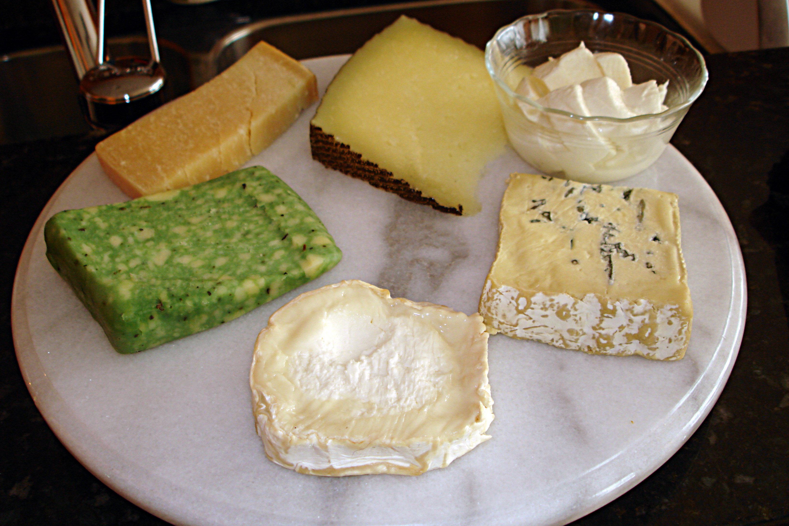 Several cheeses including blue cheese, goat's cheese and a green herb cheese on a marble board
