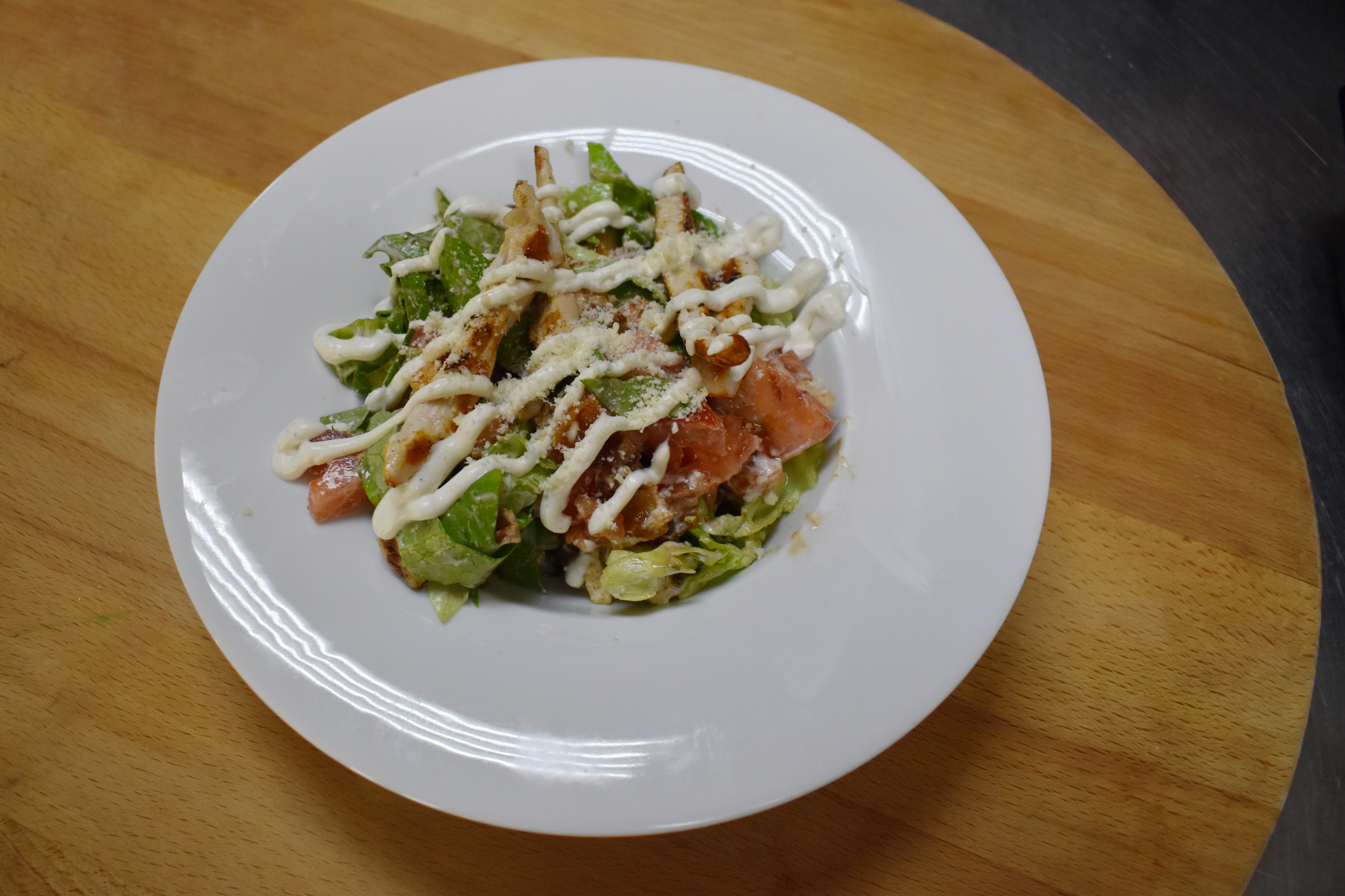 A Caesar-style salad with chicken strips, tomato and creamy dressing on a white plate