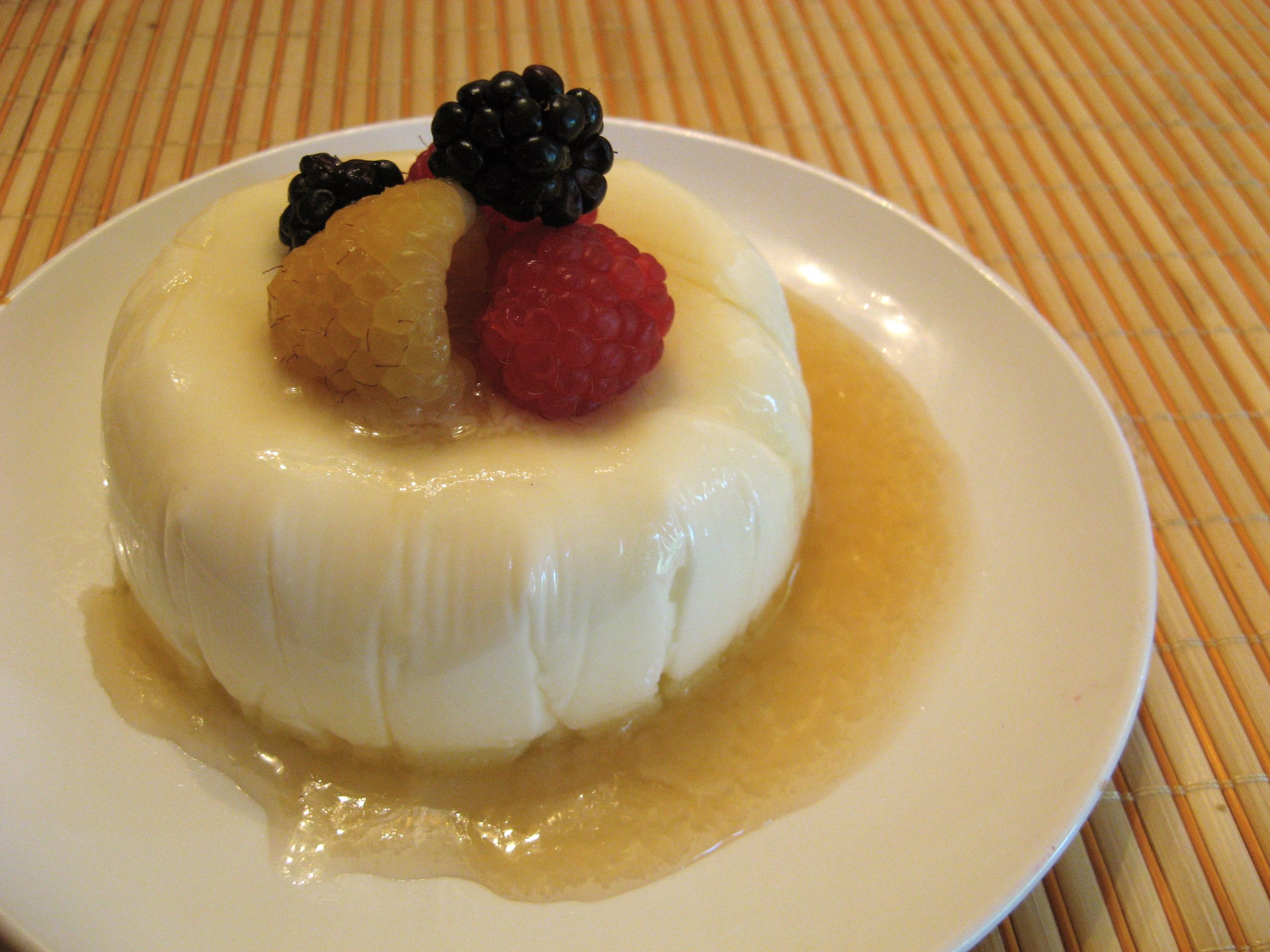 A panna cotta topped with raspberries and blackberries sitting in a pool of syrup