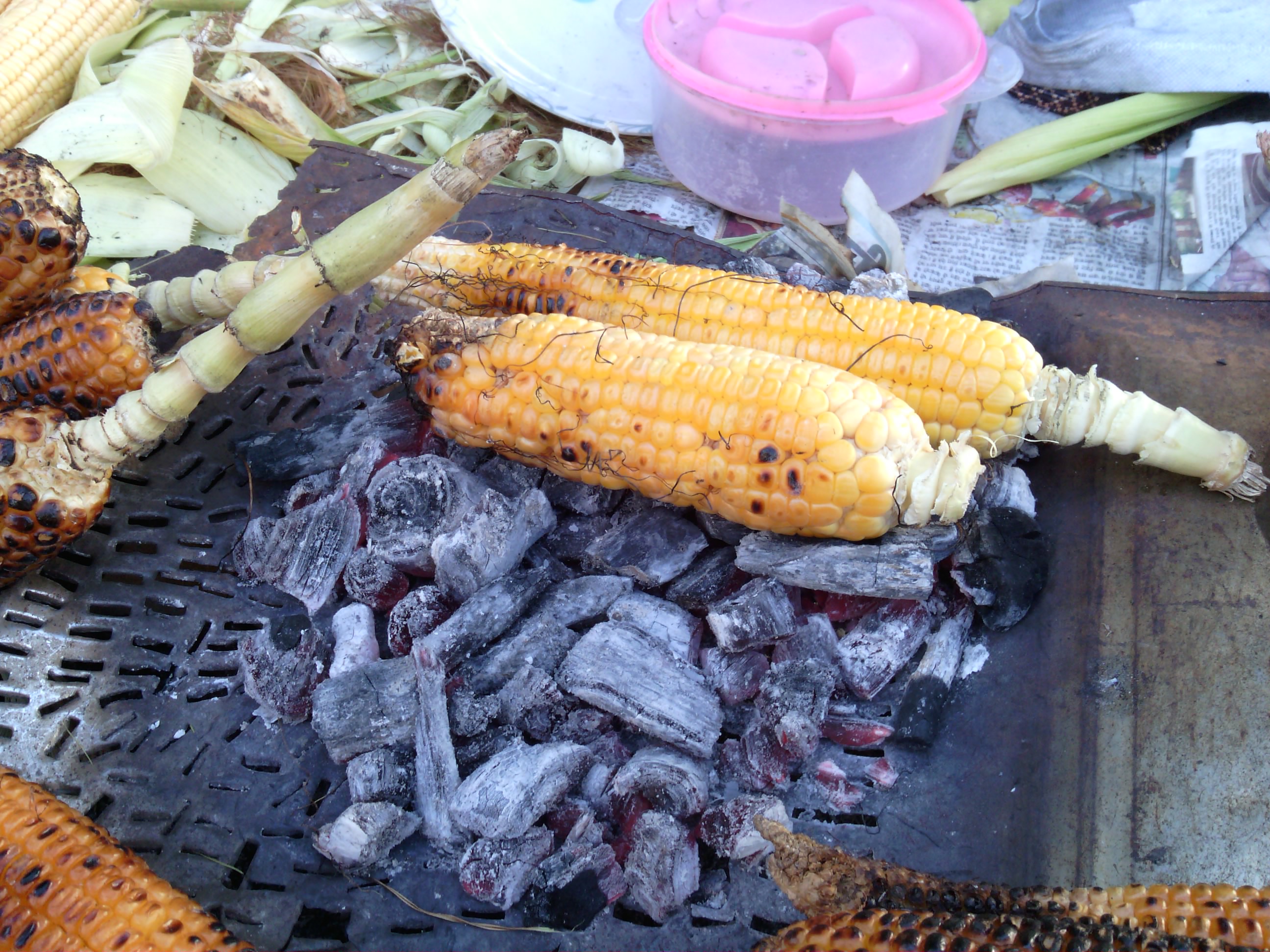 Corn on the cob roasting over glowing charcoal at an outdoor food stall