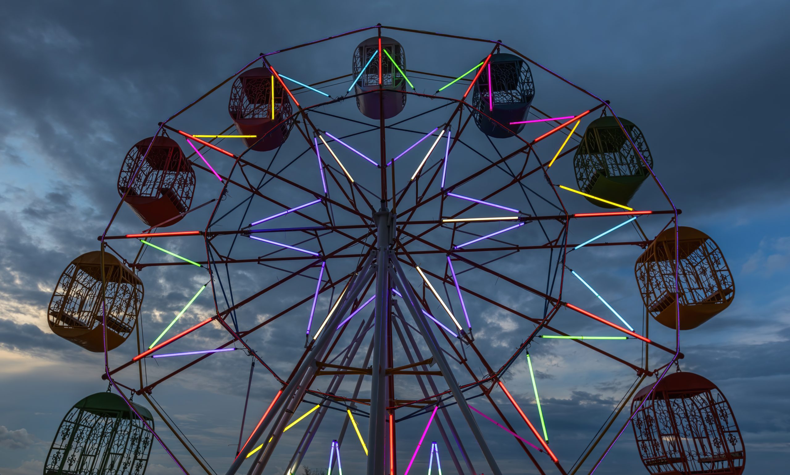 Ferris wheel with coloured gondolas lit up against a cloudy evening sky