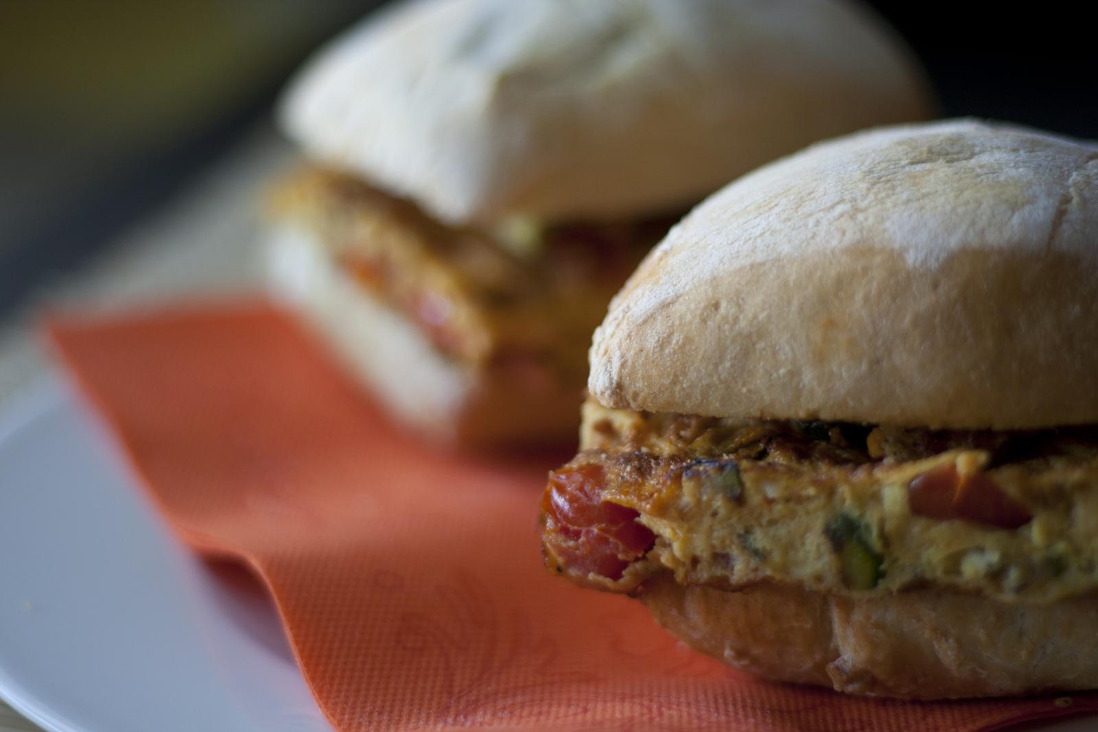 Two crusty rolls filled with vegetable omelette on an orange paper napkin