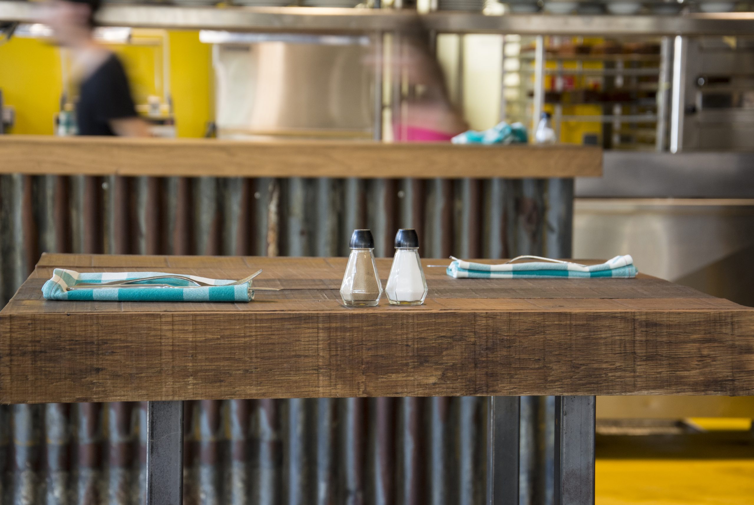 Salt and pepper shakers on a wooden restaurant table with folded napkins and cutlery