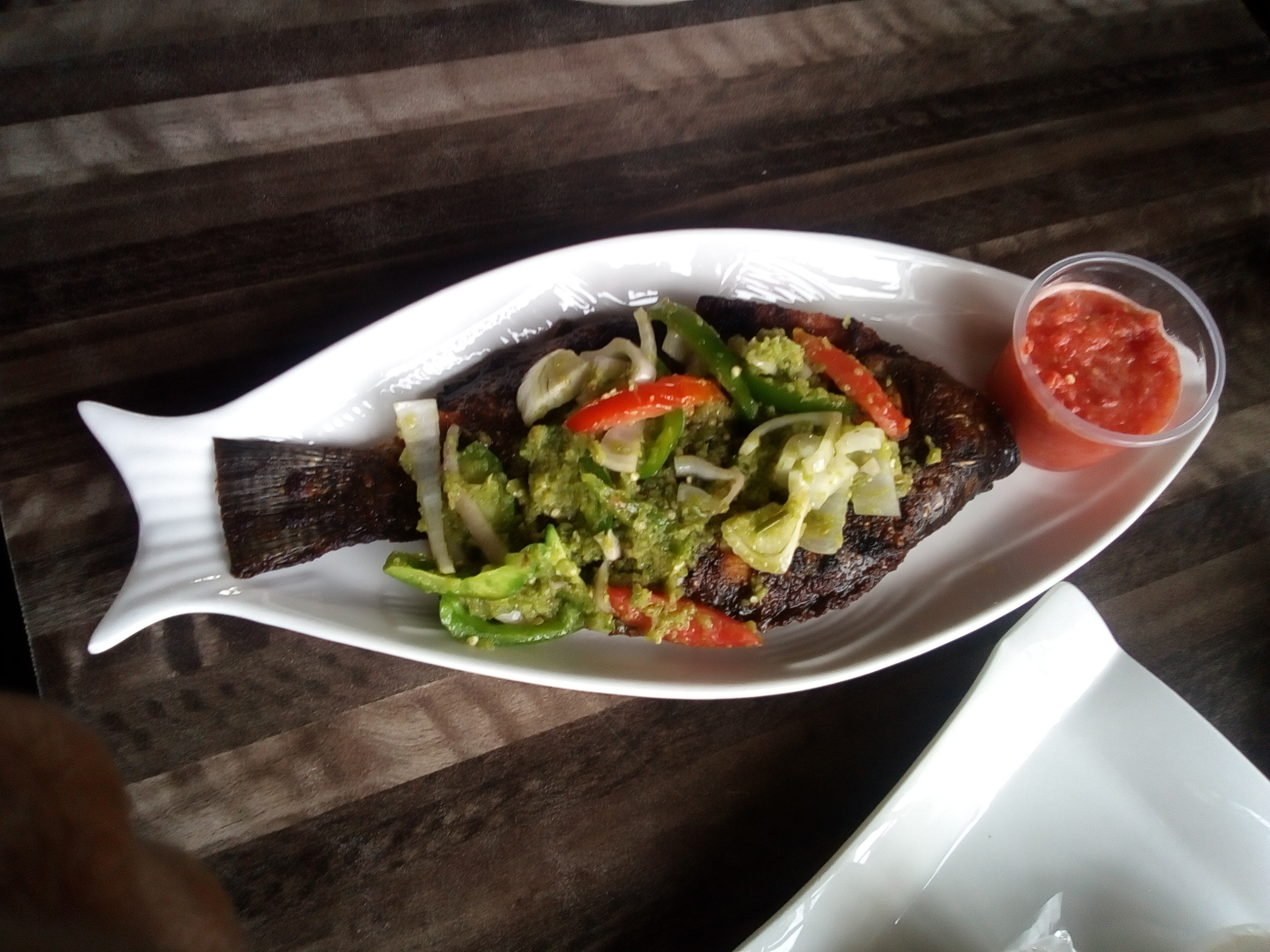 Whole grilled tilapia topped with peppers and onion on a fish-shaped plate