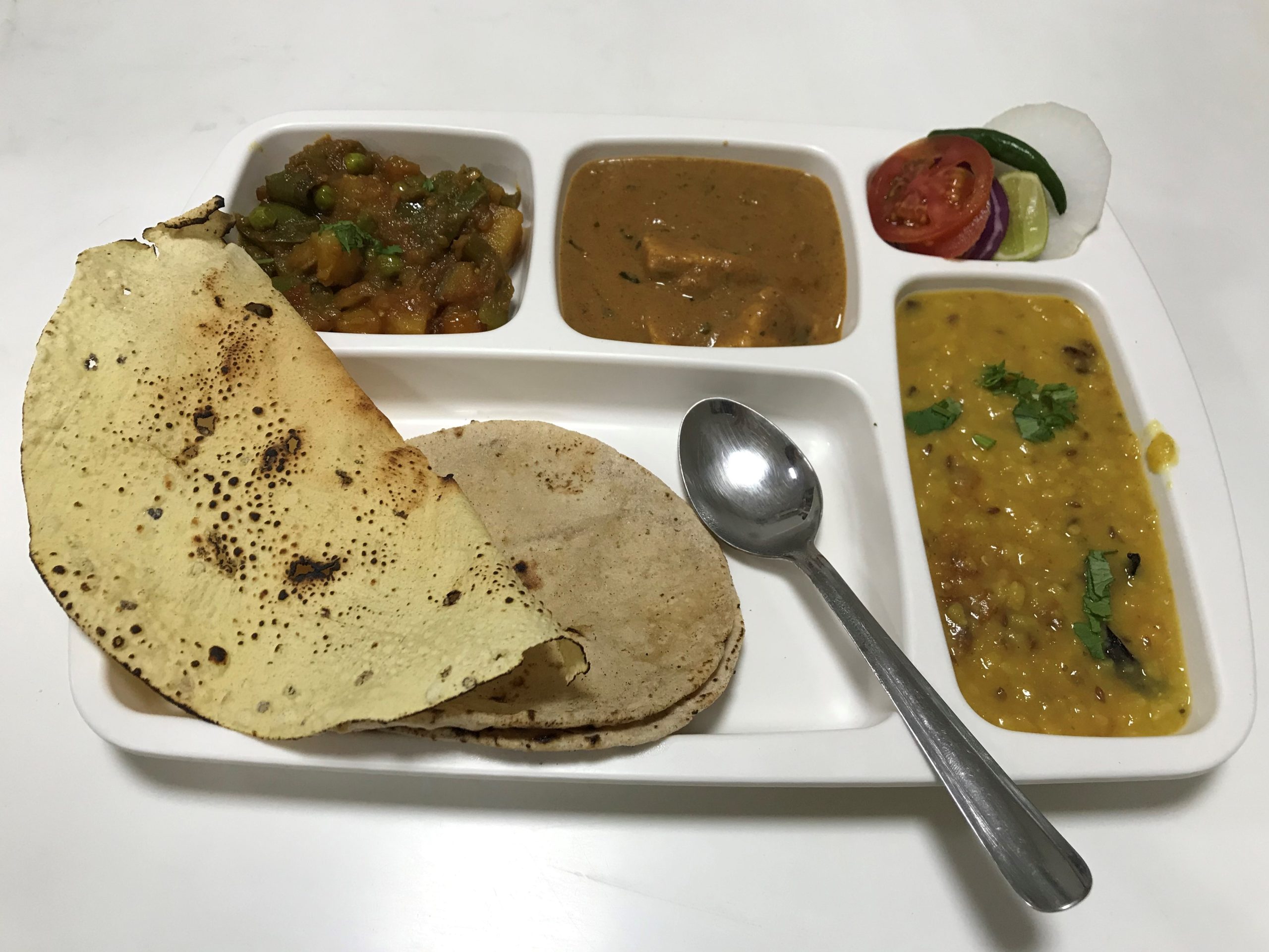 Vegetarian thali with dal, a vegetable curry, chapatis and a poppadom on a divided white tray