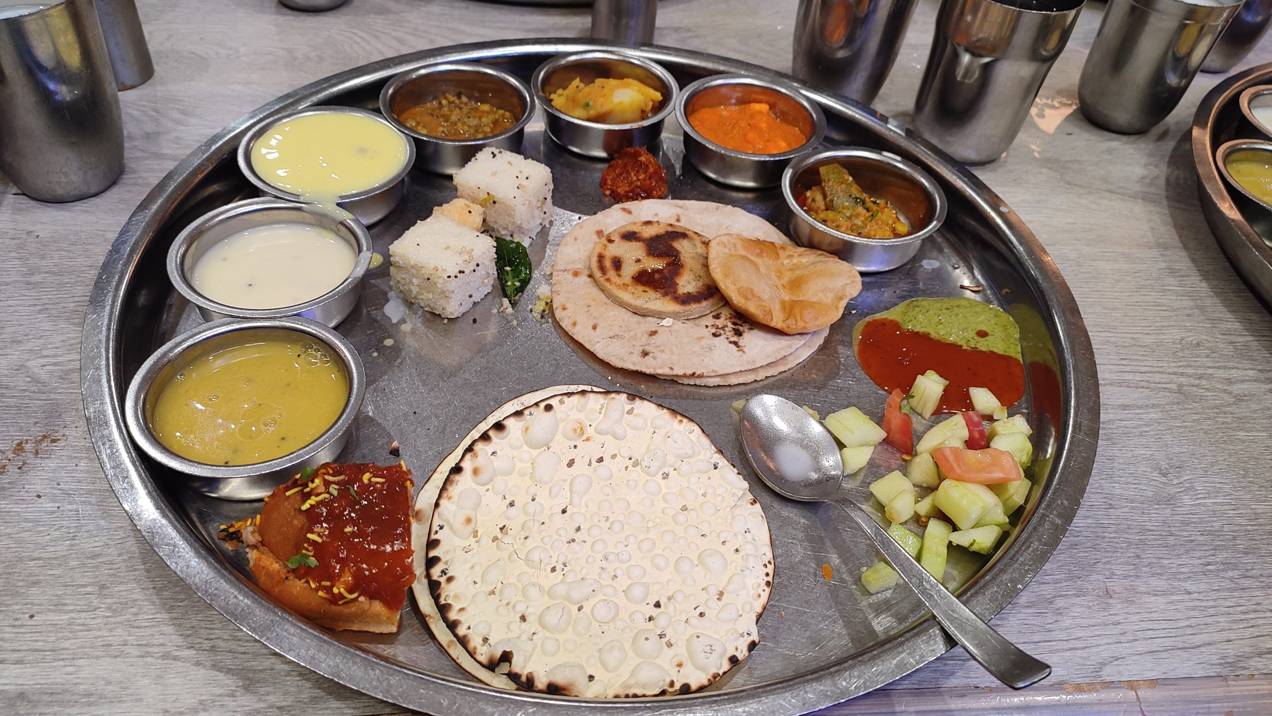 Gujarati thali on a steel platter with dal, kadhi, vegetable dishes, rotis, dhokla and salad