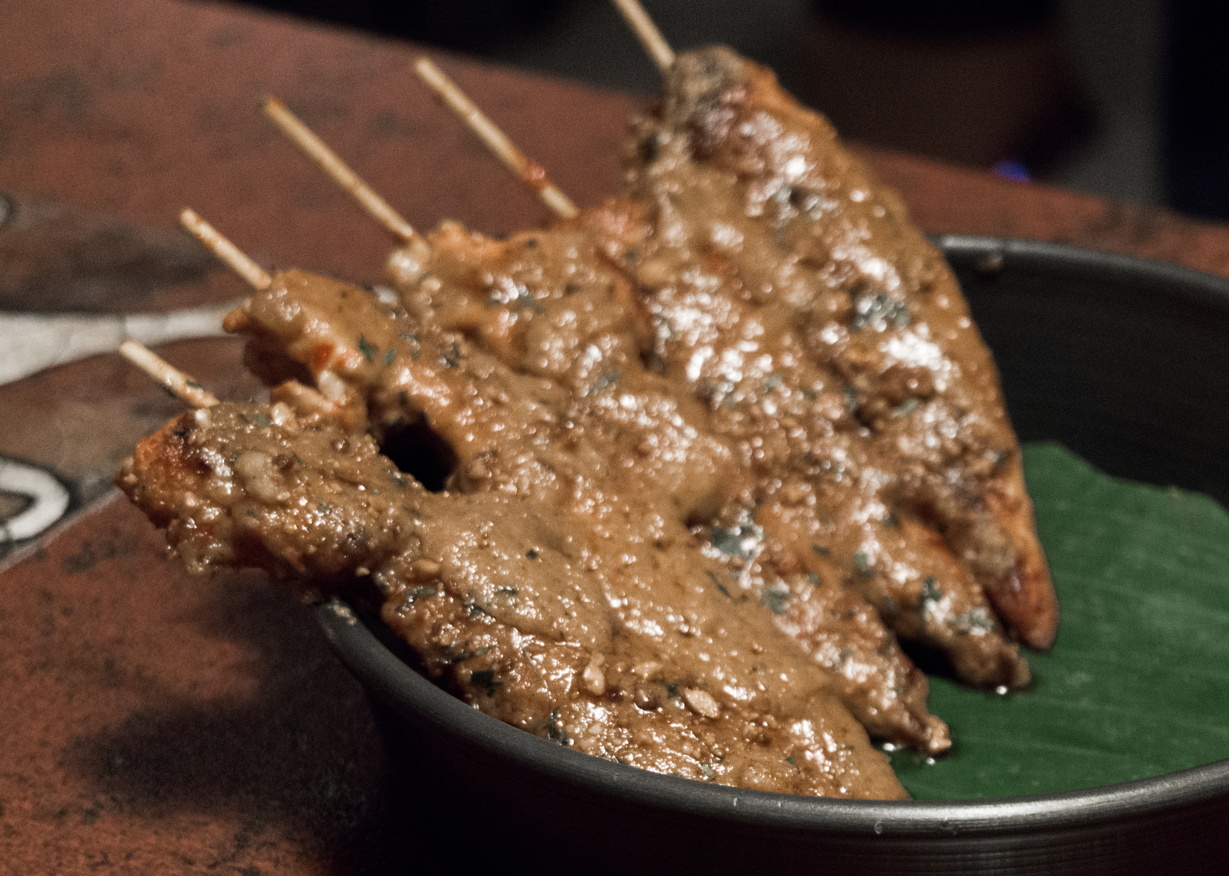 Chicken satay skewers coated in peanut sauce on a banana leaf