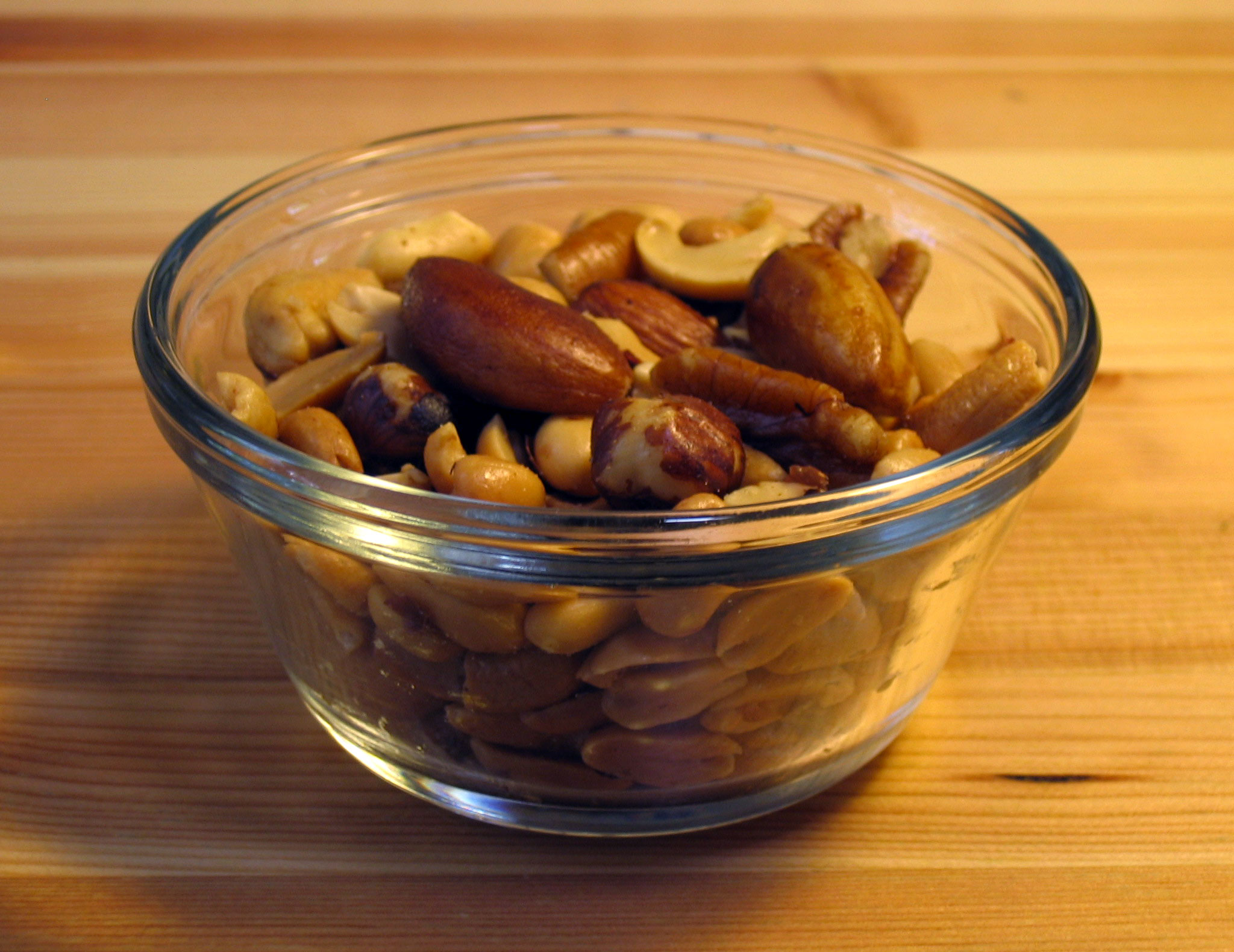 Small glass bowl of mixed nuts including almonds, cashews, Brazil nuts and peanuts on a wooden table