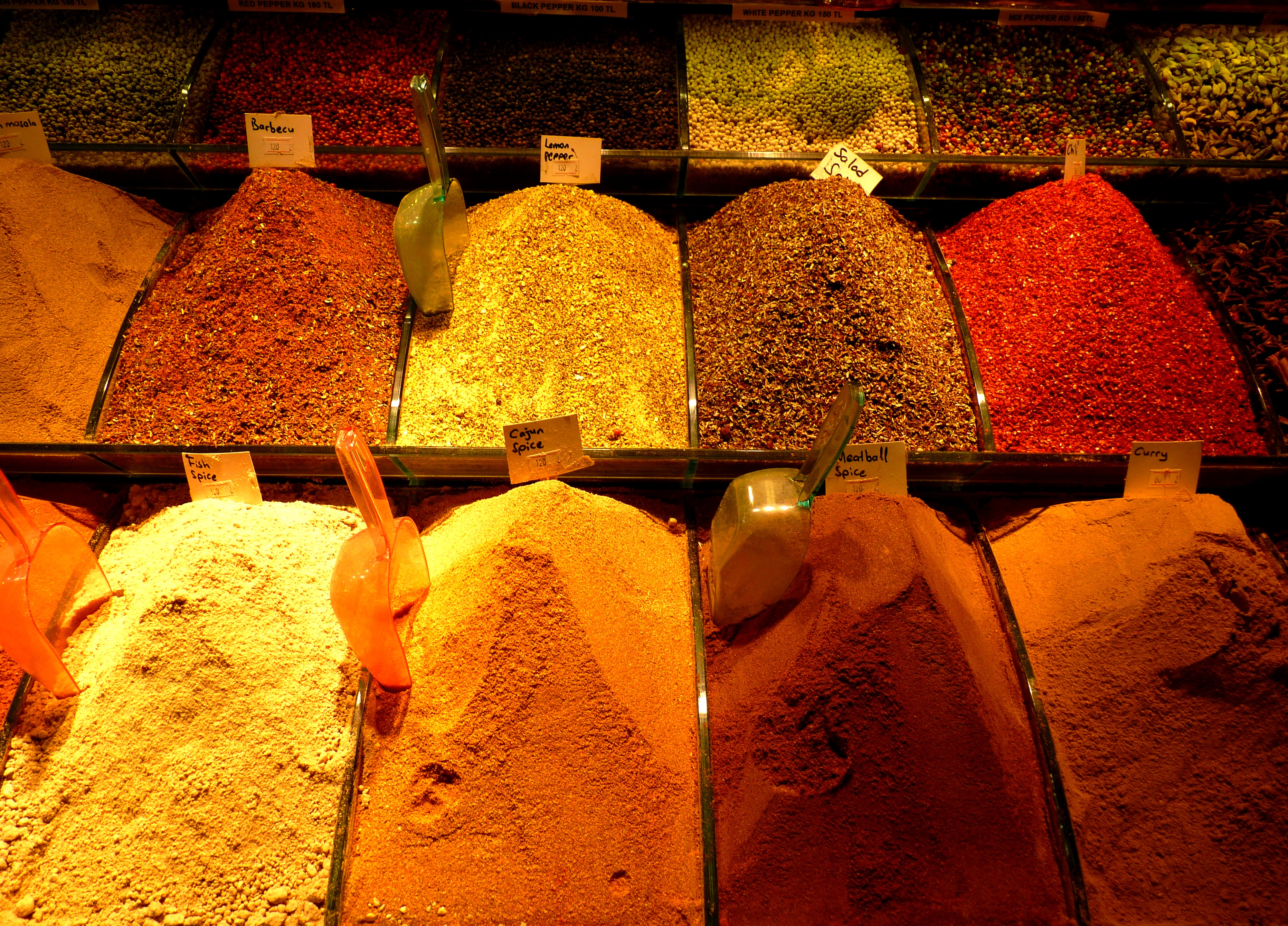 Mounds of ground spices in a market display with handwritten labels and plastic scoops