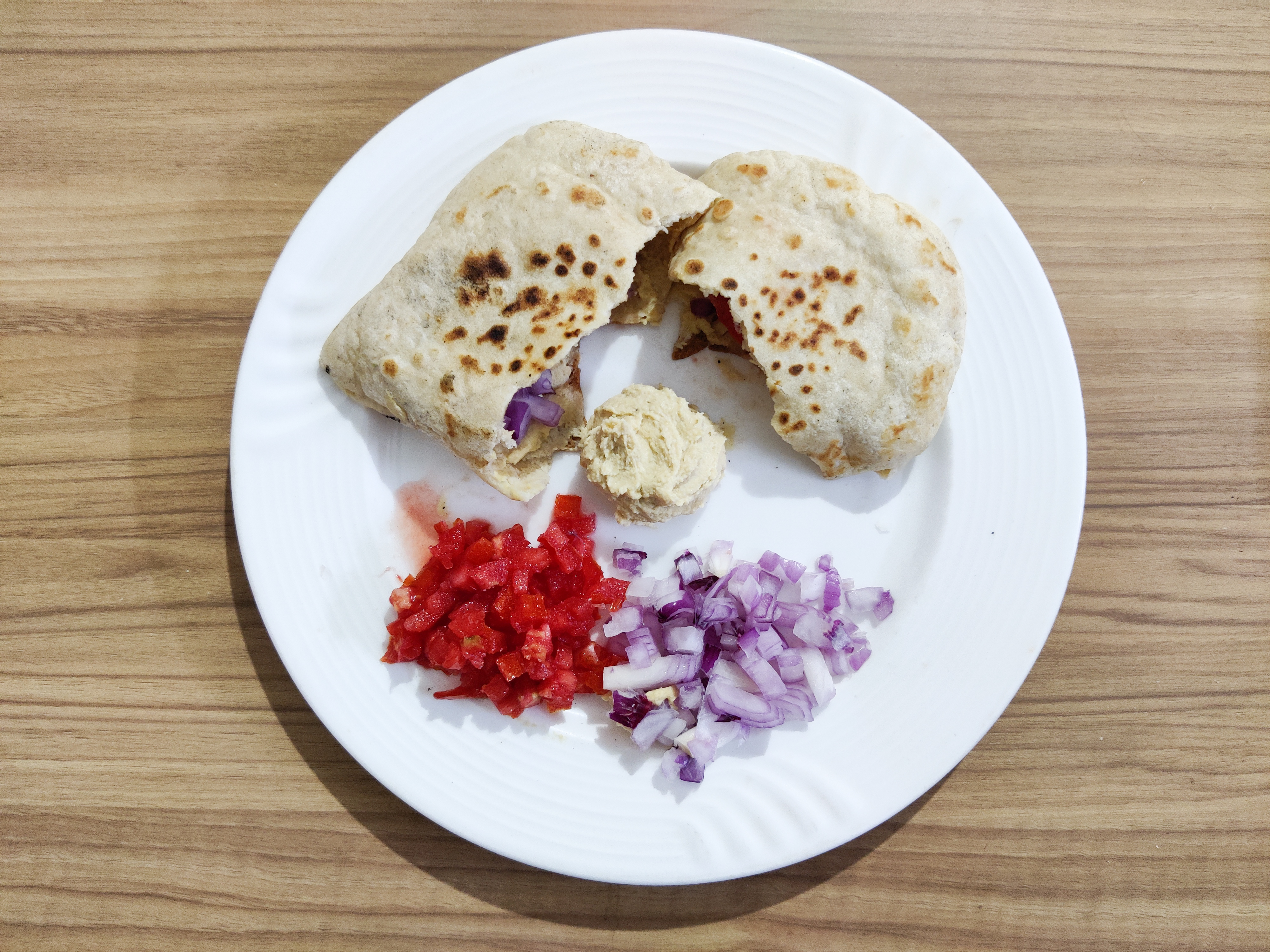 Hummus and warm pita bread on a plate with chopped red pepper and onion