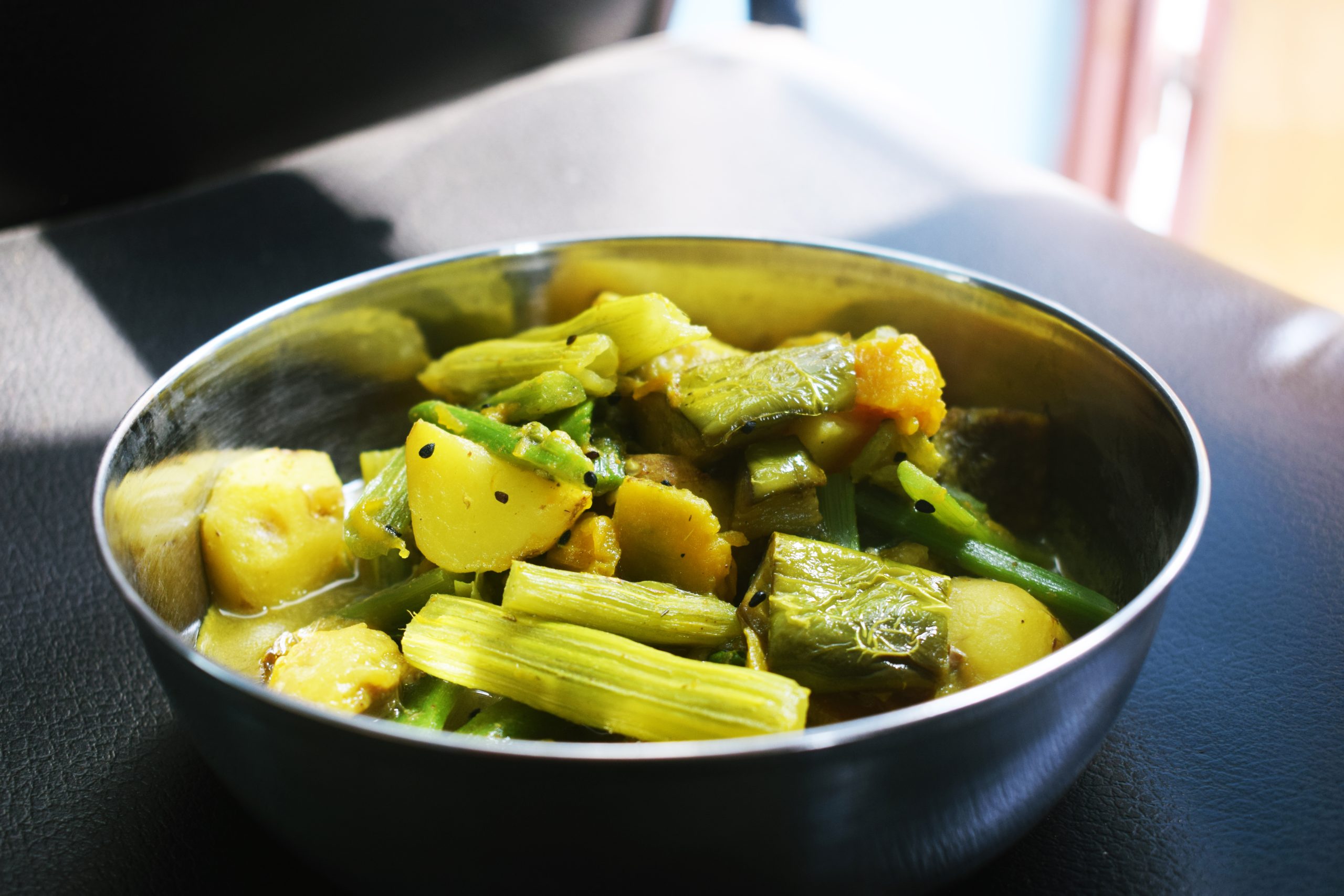 A metal bowl of mixed vegetable curry with potato, beans and courgette